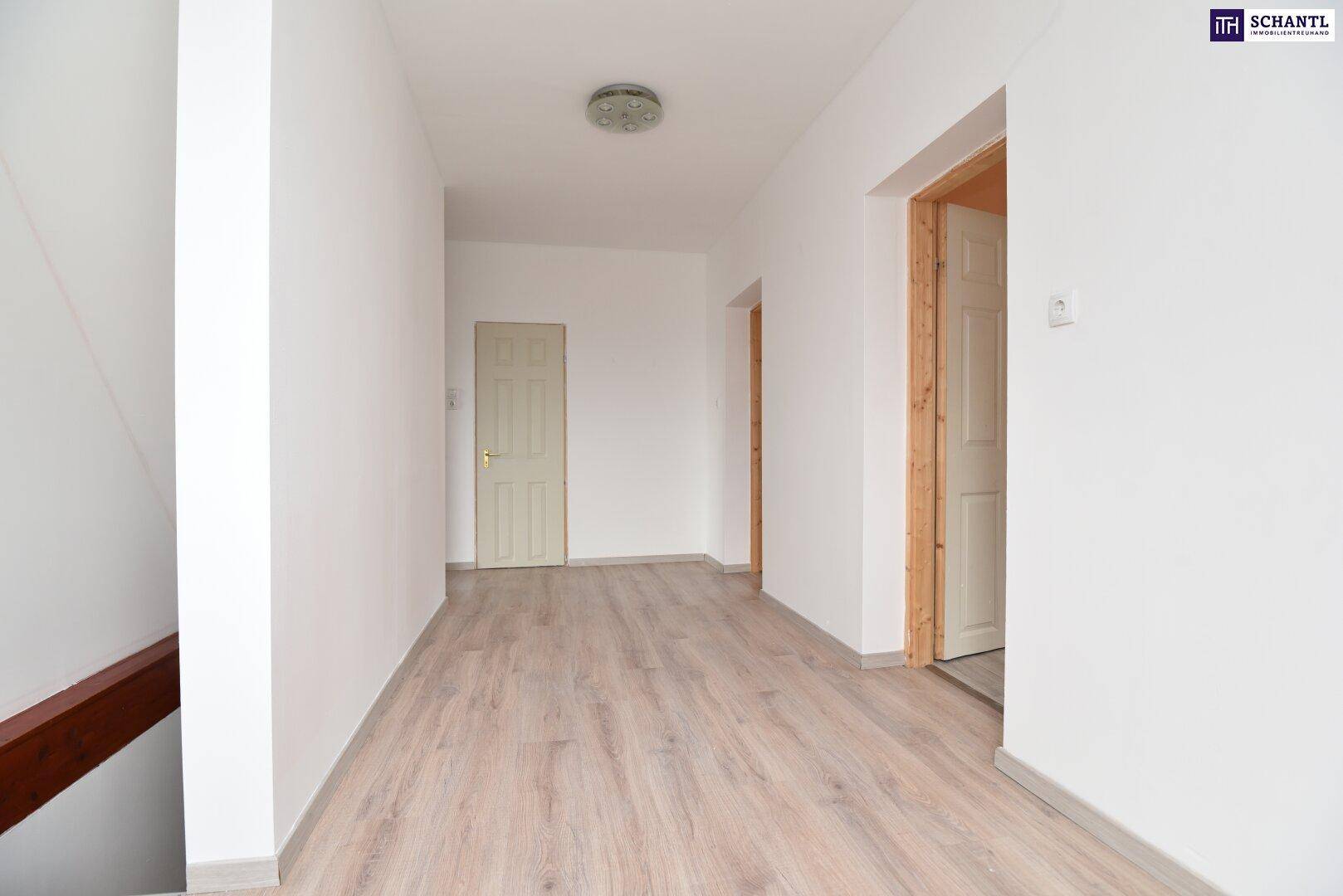Heller Flur mit Laminatboden, weißen Wänden und Holztürrahmen, der zu weiteren Räumen führt.