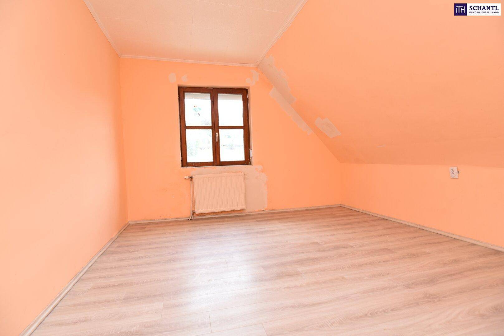 Dachgeschosszimmer mit schrägen Wänden, hellem Laminatboden, pfirsichfarbenen Wänden und einem Fenster.