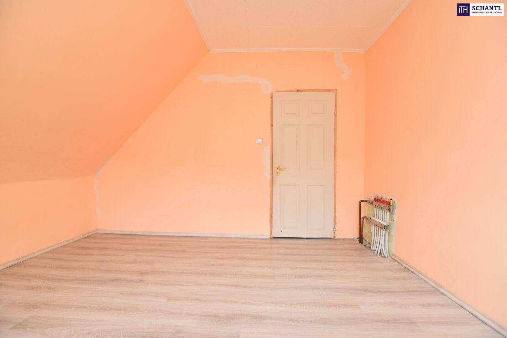 Dachgeschosszimmer mit hellem Laminatboden, pfirsichfarbenen Wänden und einer schlichten Holztür.