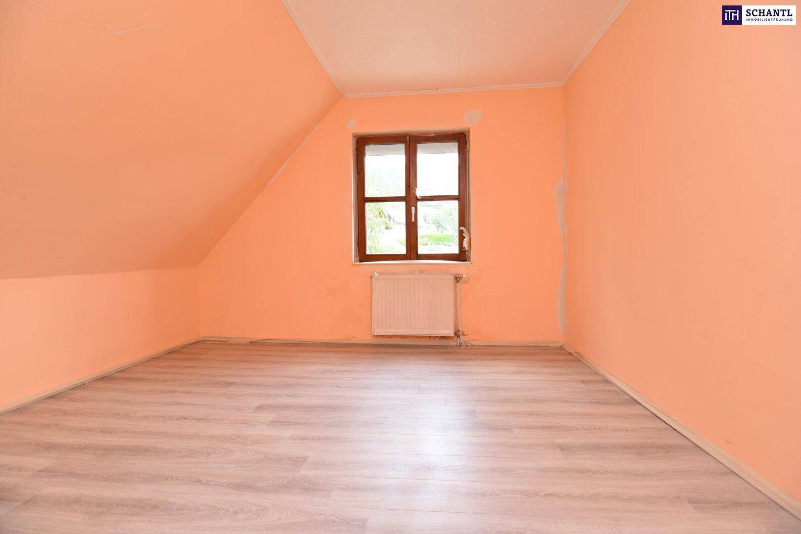 Dachgeschosszimmer mit schrägen Wänden, hellem Laminatboden, pfirsichfarbenen Wänden und einem Fenster.