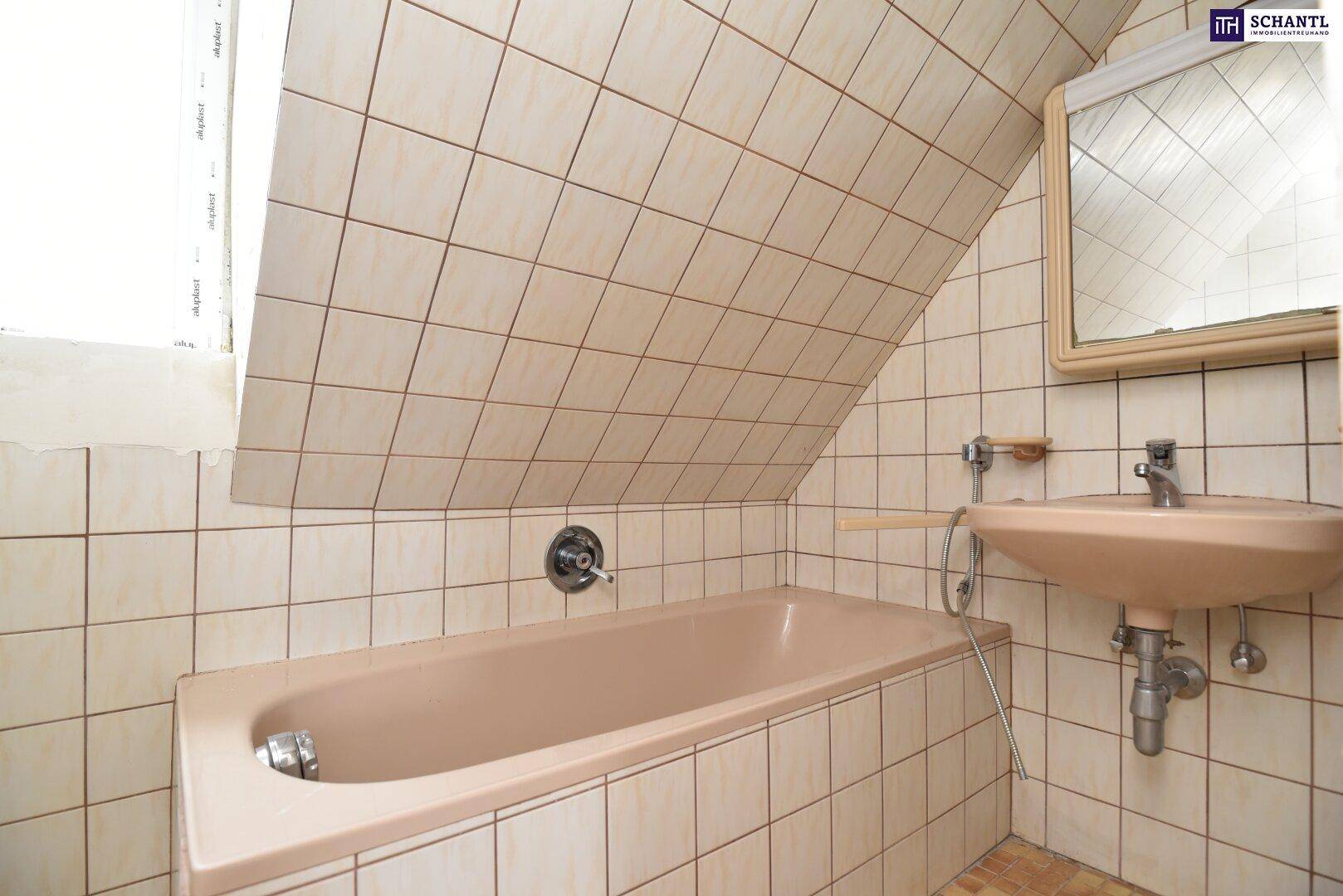 Badezimmer mit Badewanne, Waschbecken, Spiegel und schrägen Wänden, gefliest in beigen Tönen.