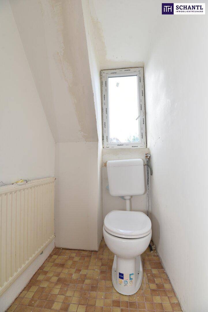 Kleines WC mit Toilette, gefliestem Boden, weißen Wänden, schräger Decke und einem Fenster.