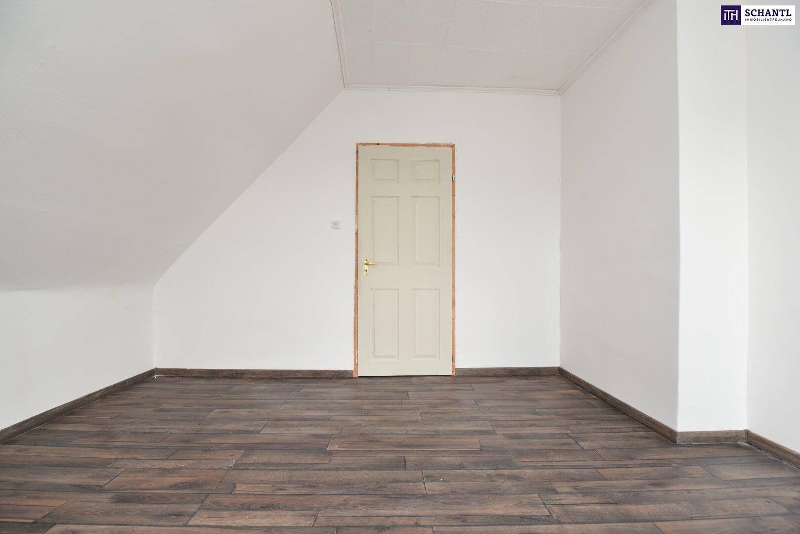 Leeres Dachgeschosszimmer mit dunklem Holzboden, weißen Wänden und einer schlichten Holztür.