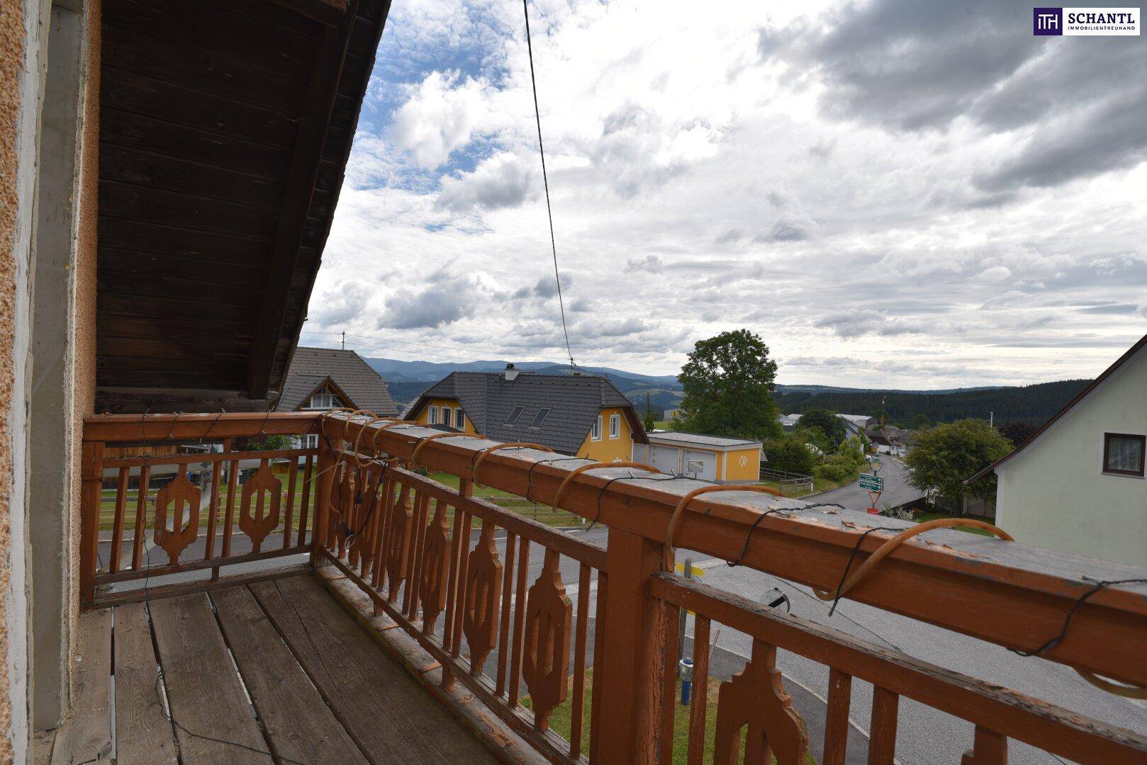Balkon mit traditionellem Holzgeländer und weitem Blick über die ländliche Umgebung an einem bewölkten Tag.