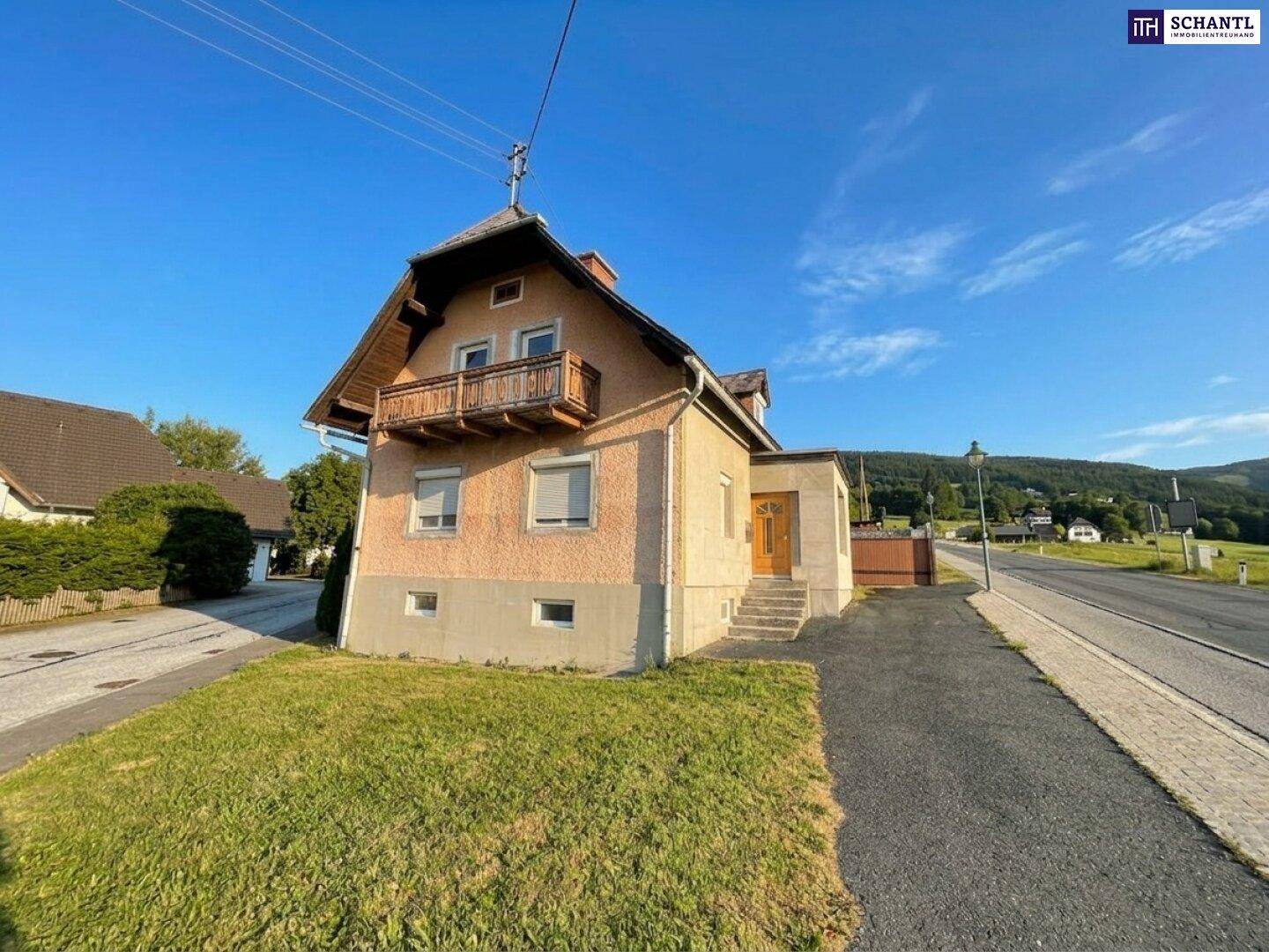 Traditionelles Haus mit Balkon und Satteldach, umgeben von Rasenflächen unter strahlend blauem Himmel.