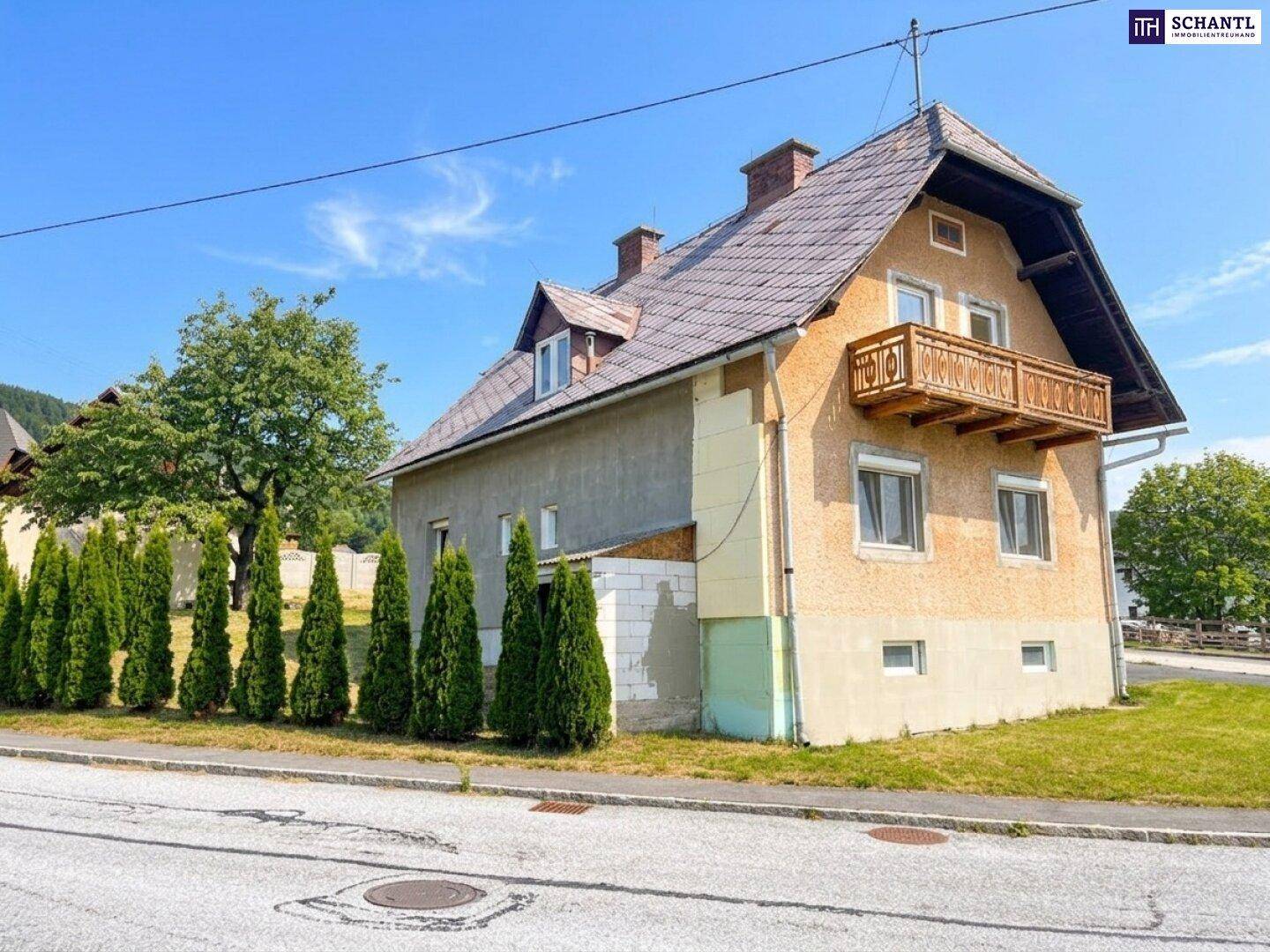 Seitenansicht eines Hauses mit Balkon und einer Reihe von Nadelbäumen entlang der Grundstücksgrenze.
