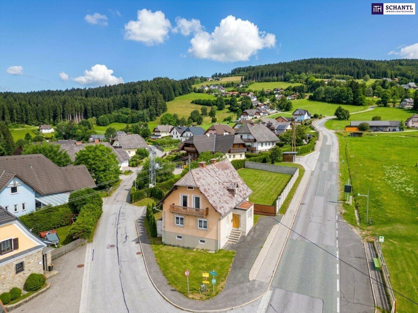 Luftaufnahme eines charmanten Dorfes mit traditionellen Häusern, umgeben von grünen Feldern und Wäldern.