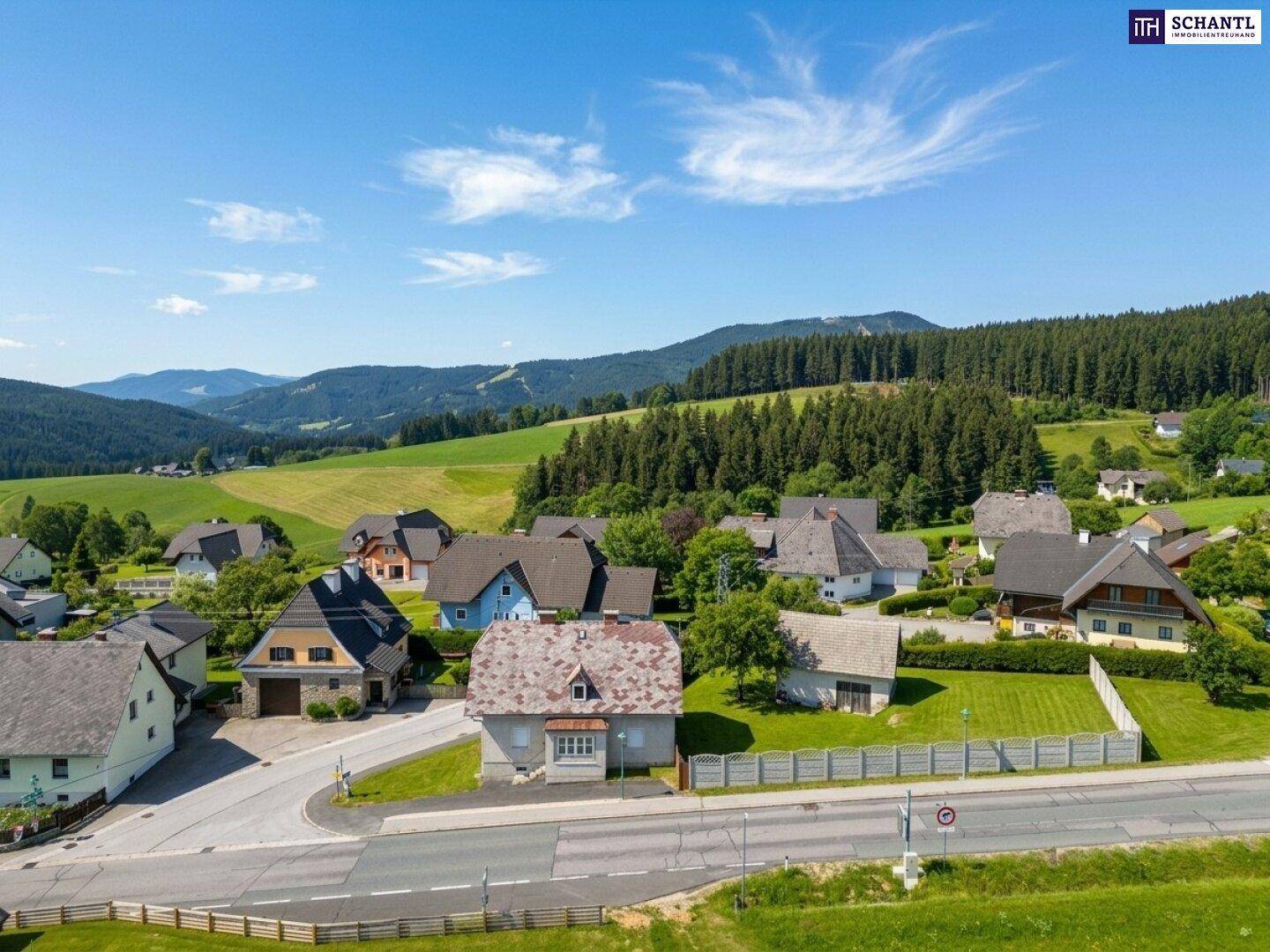Malerische Luftaufnahme eines Dorfes in ländlicher Umgebung mit grünen Hügeln und Wäldern.
