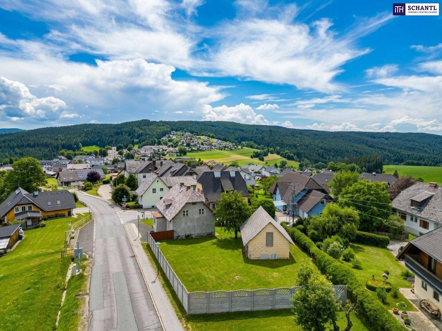 Panoramablick auf ein idyllisches Dorf, eingebettet in eine grüne Hügellandschaft mit weitem Himmel.