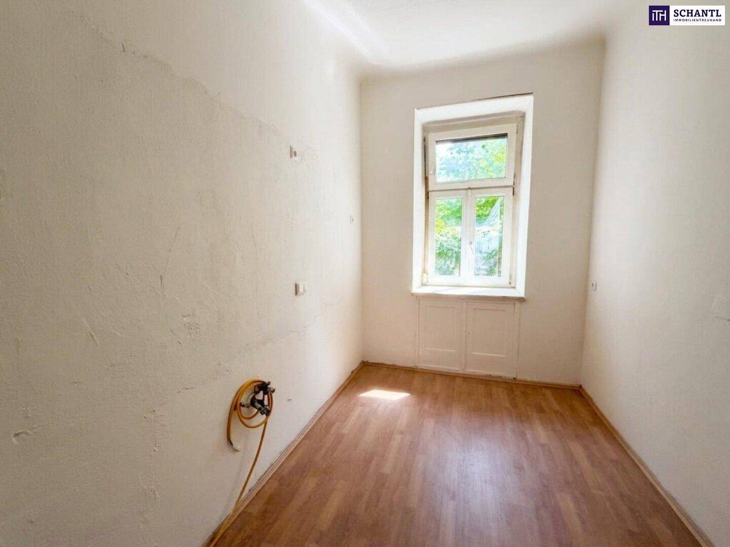 Leerer Raum mit Laminatboden und einem Fenster, vorbereitet für eine Kücheninstallation.