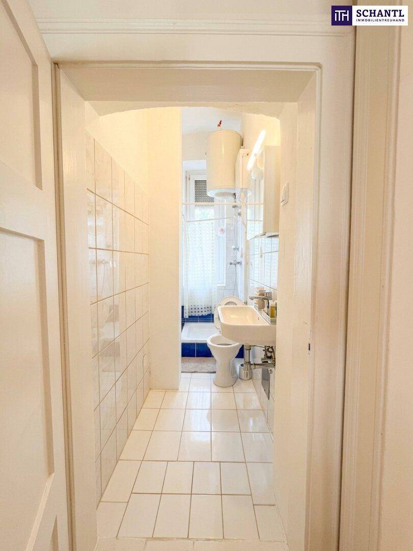 Schmaler Badezimmerbereich mit weißen Fliesen, Waschbecken, Toilette und Duschbereich.