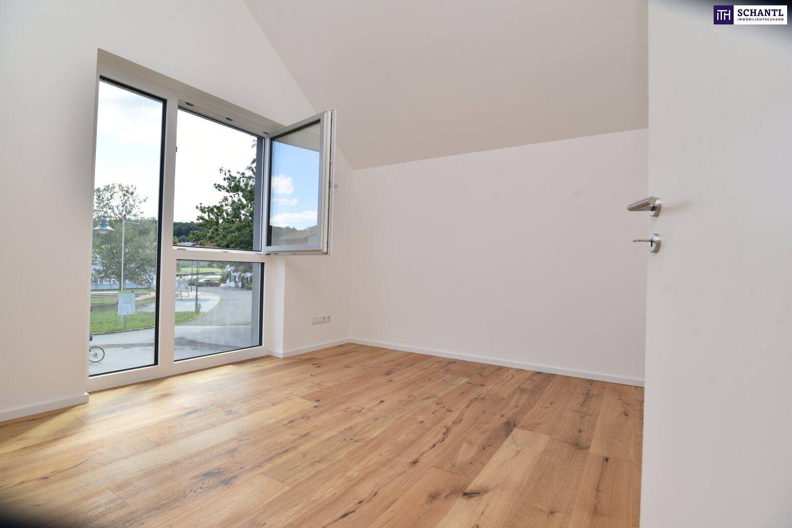 Lichtdurchflutetes Zimmer mit großen Fenstern, Holzboden und einem angenehmen Blick ins Grüne.