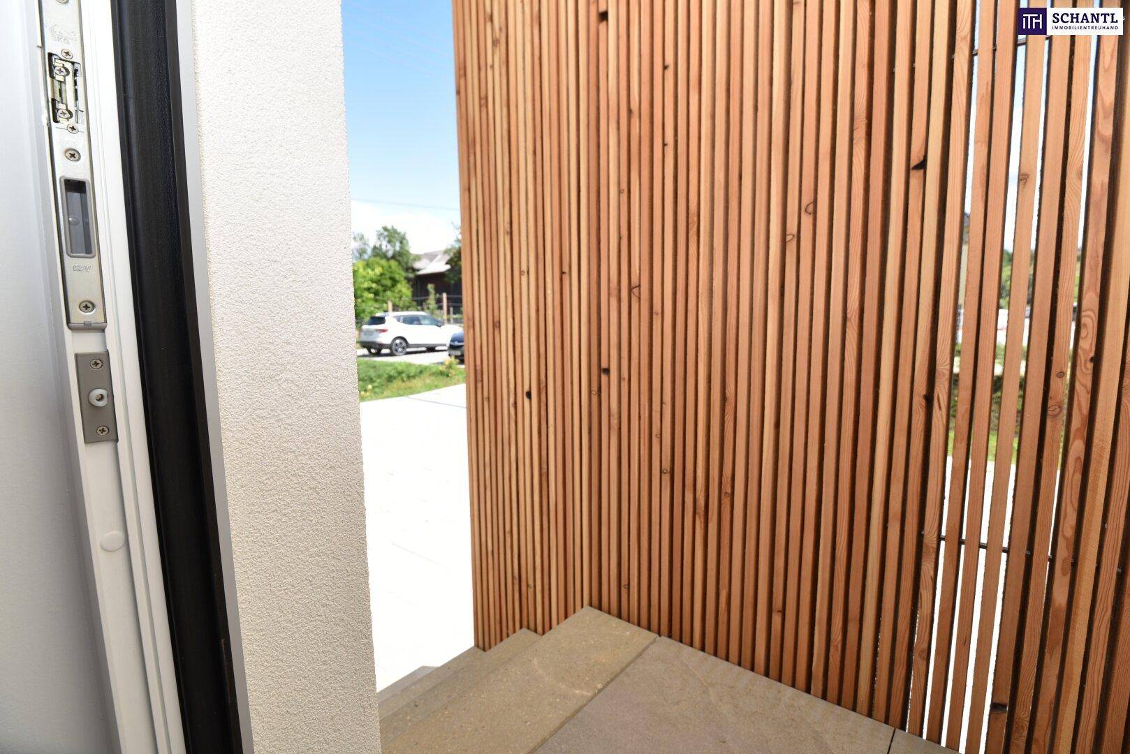 Detailansicht des Hauseingangs mit Holzelementen und einem Blick auf die ruhige Umgebung.