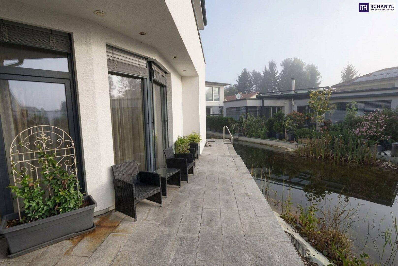 Gepflasterte Terrasse mit Sitzgelegenheiten direkt am Teich, umgeben von moderner Architektur und viel Grün.