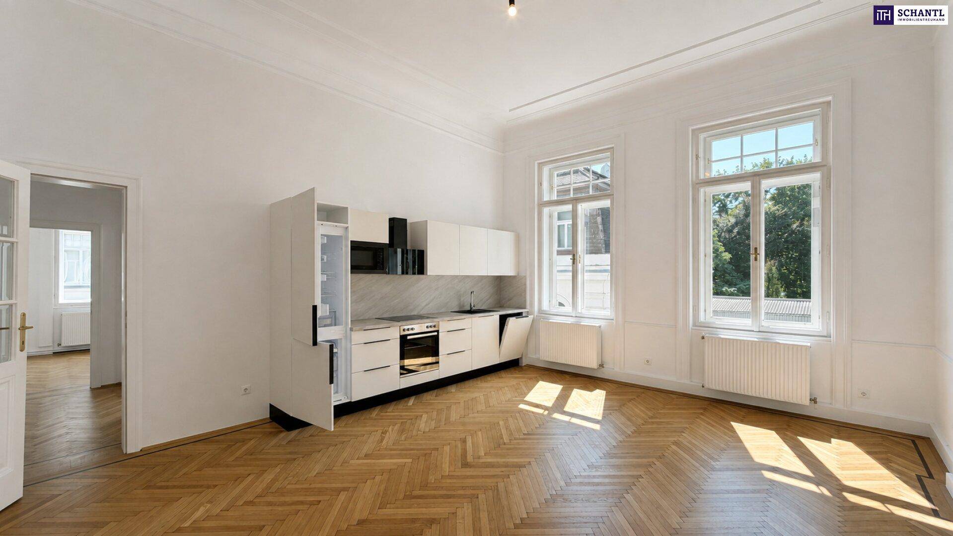 Helle Wohnküche mit integrierten Geräten, weißen Schränken und klassischem Fischgrätparkett, lichtdurchflutet durch hohe Fenster.