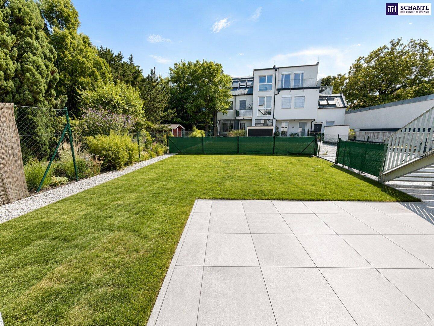 Gepflegter Gartenbereich mit großer Terrasse und Blick auf die moderne Wohnanlage.