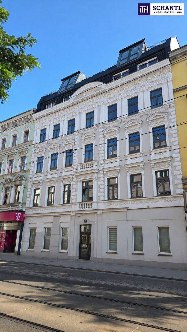 Historische Fassade eines Mehrfamilienhauses mit modernem Dachausbau und großen Fenstern zur Straße.