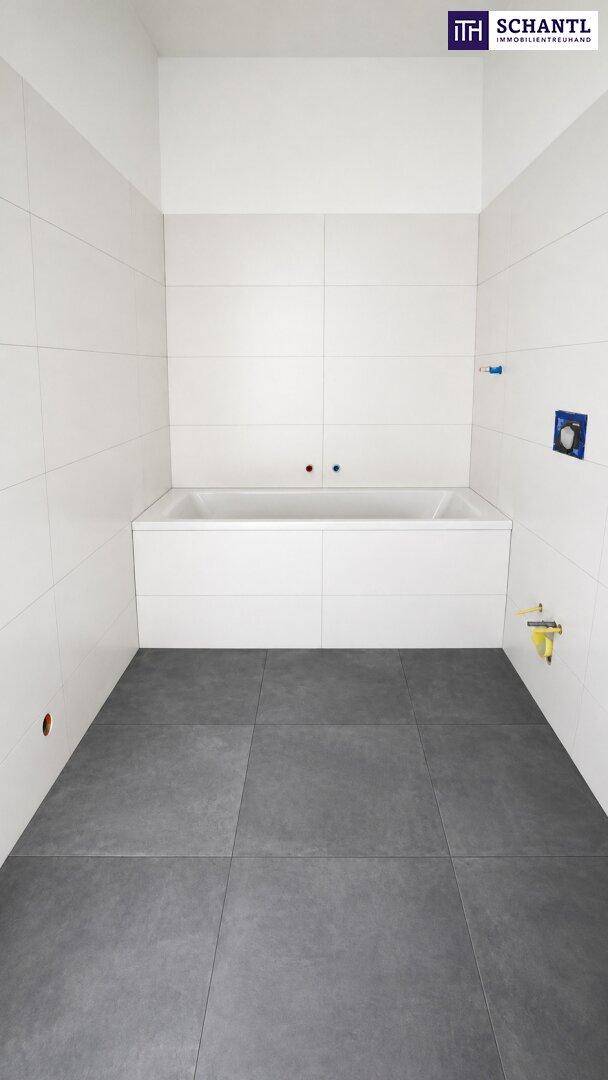 Unfertiges Badezimmer mit eingebauter Badewanne, grauen Bodenfliesen und weißen Wandfliesen.