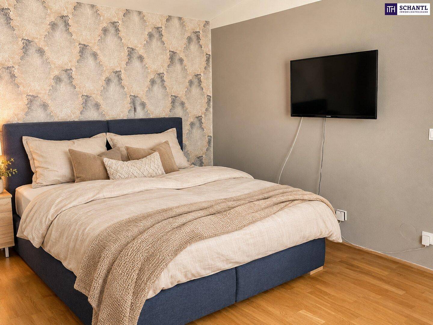 Gemütliches Schlafzimmer mit Doppelbett, gemusterter Tapete und an der Wand montiertem Fernseher.