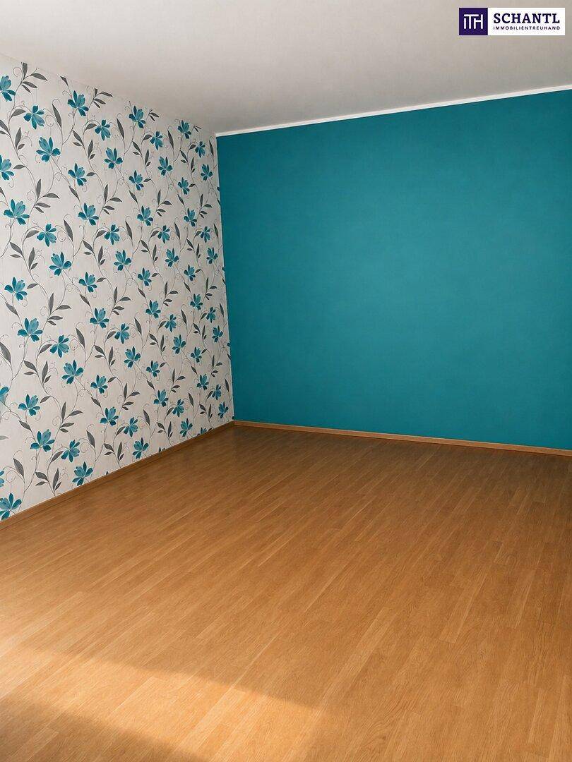 Leeres Zimmer mit farbenfroher Wandgestaltung, floraler Tapete und hellem Parkettboden.
