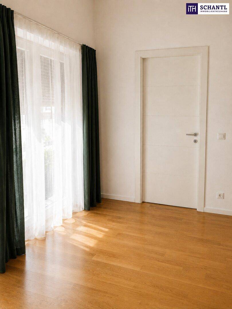 Leeres Zimmer mit hellem Parkettboden, weißen Wänden und großen Fenstern mit Vorhängen.