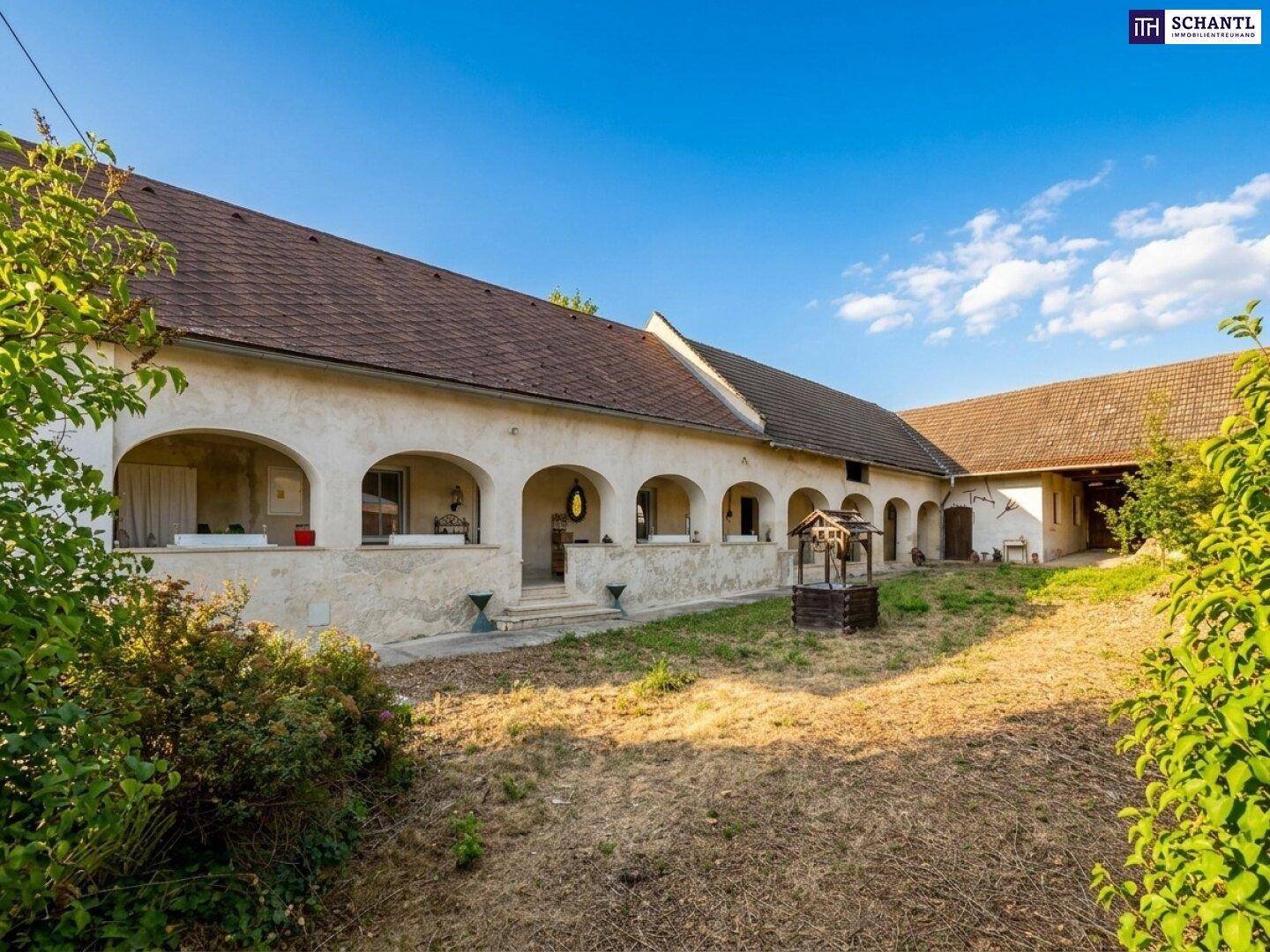 Innenhof des Anwesens mit Arkadengang und einem alten Brunnen, umgeben von Natur.