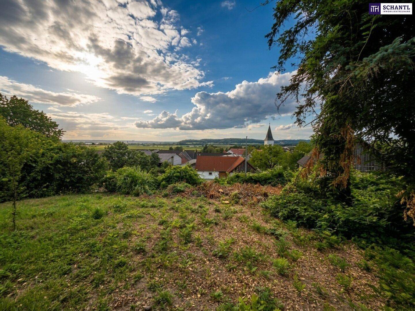 Weitläufiger Blick über die ländliche Umgebung mit einem Dorf und Kirchturm am Horizont.