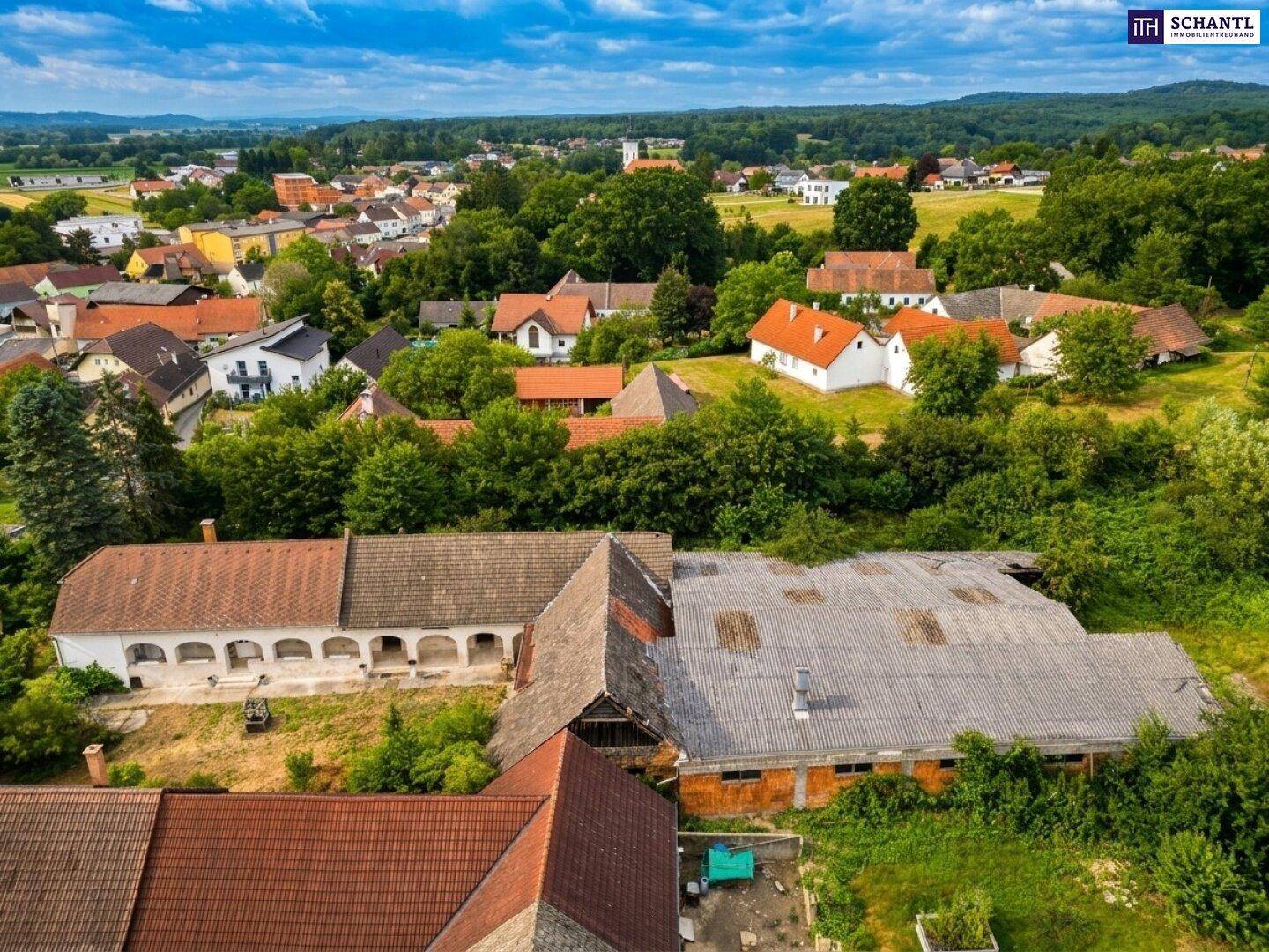 Weitläufige Luftaufnahme des Dorfes mit seinen Häusern, umgeben von Feldern und Wäldern.