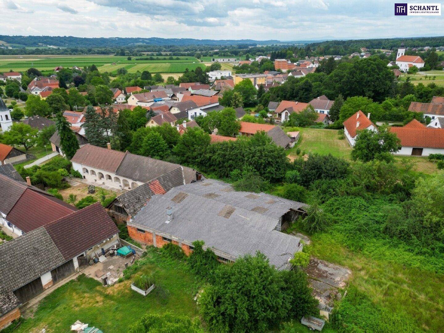 Luftaufnahme der ländlichen Siedlung mit verschiedenen Gebäuden und viel Grün.
