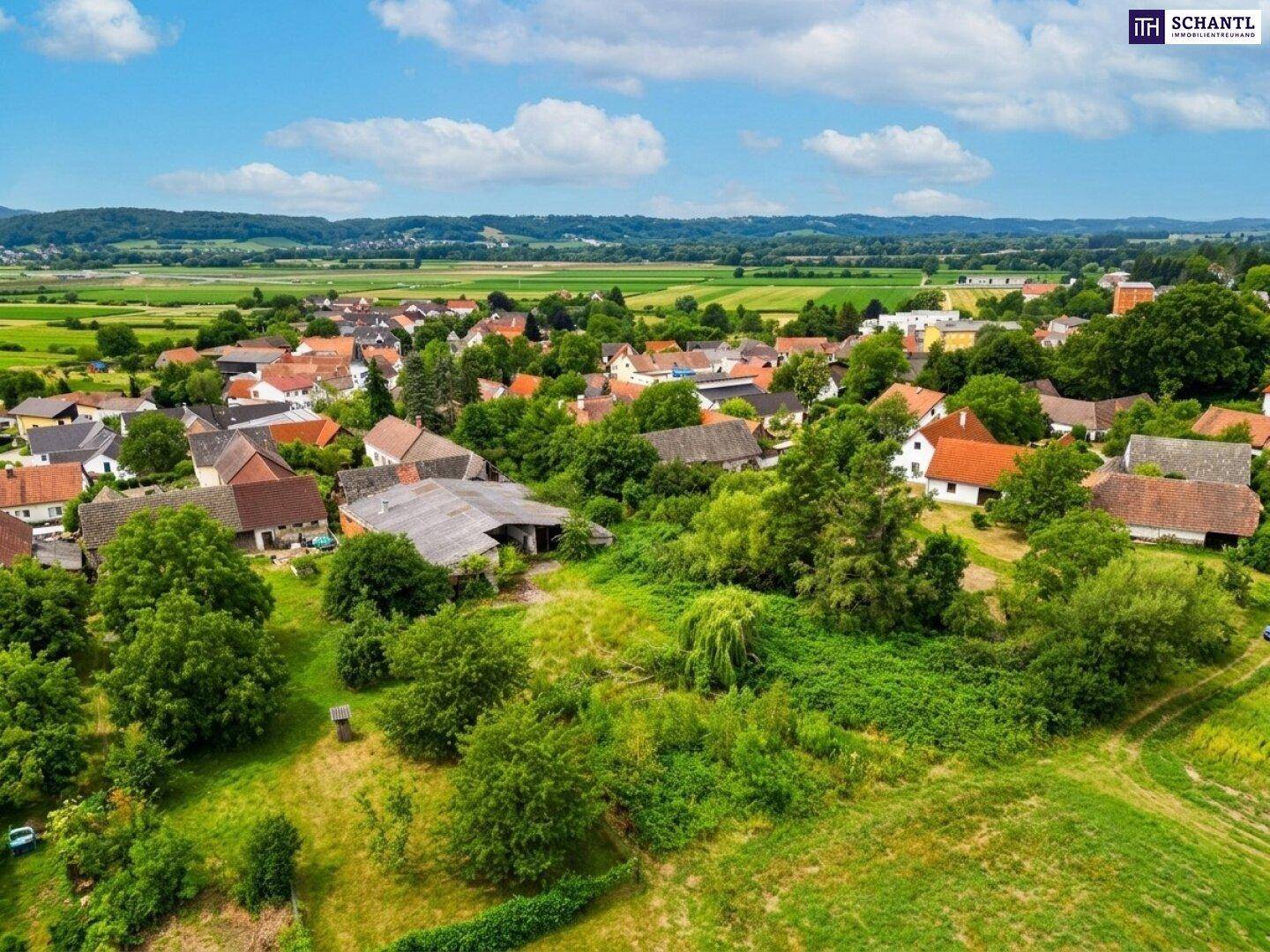 Panoramablick über die weite, grüne Landschaft mit einem kleinen Dorf im Hintergrund.