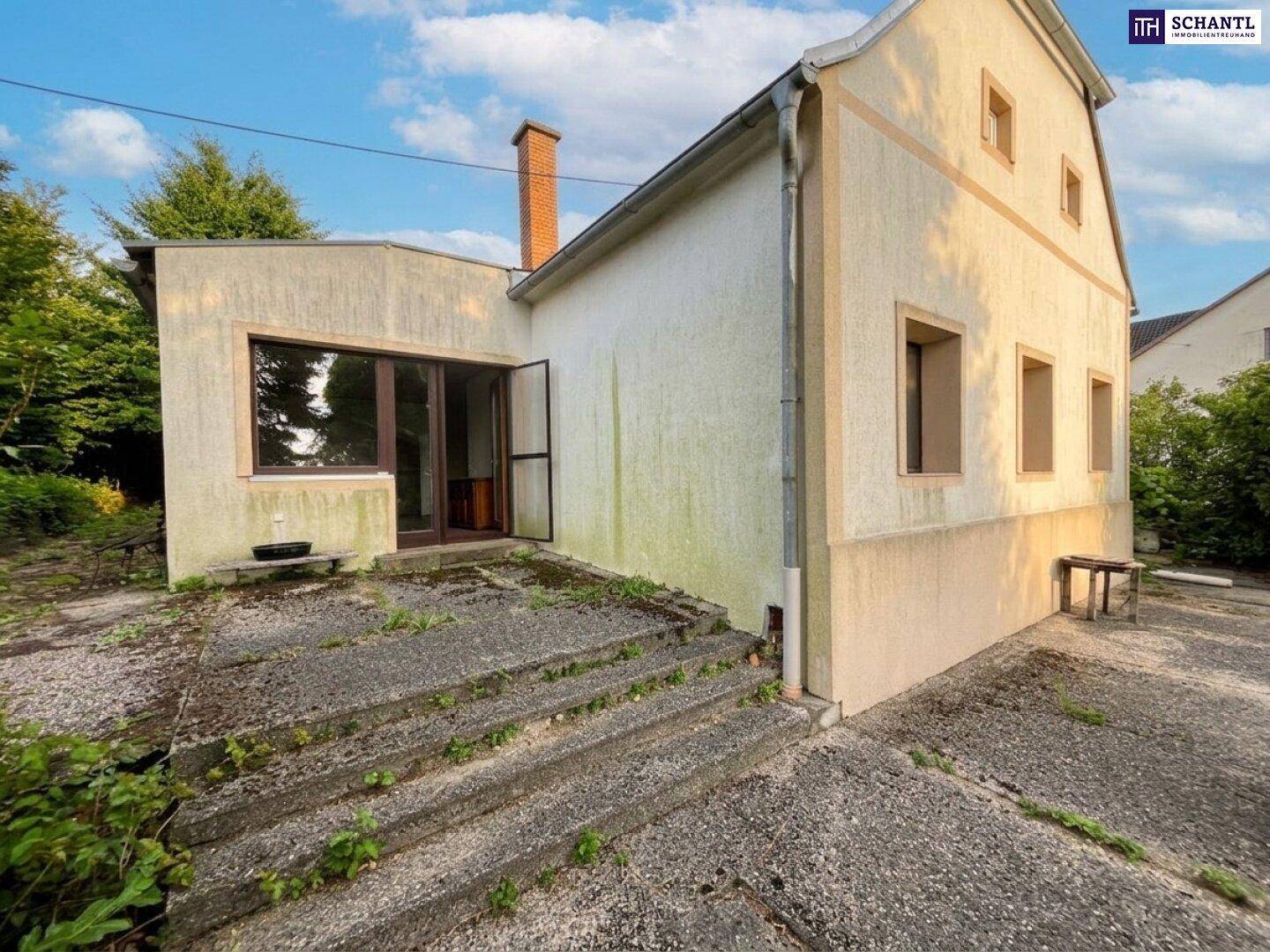 Seitenansicht des Hauses mit Außentreppe und einem Anbau, umgeben von viel Grün.