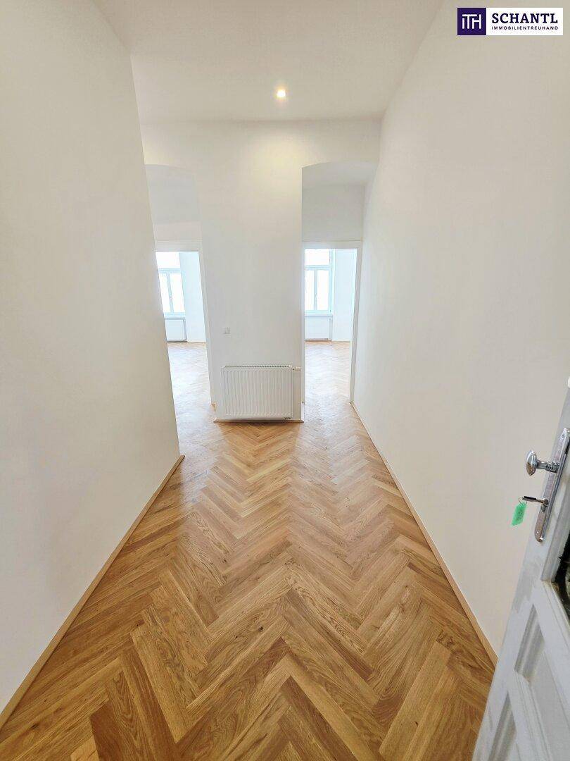 Langer, heller Flur mit Fischgrätparkett, der zu den verschiedenen Zimmern der Wohnung führt.