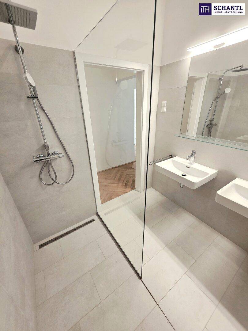 Zeitgemäßes Badezimmer mit ebenerdiger Dusche, zwei Waschbecken und hellen Fliesen.