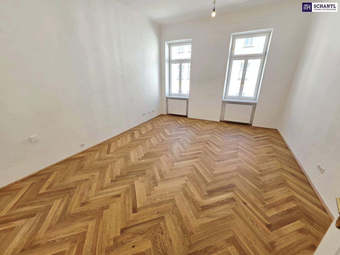 Geräumiges Zimmer mit klassischem Fischgrätparkett und viel Tageslicht durch die großen Fenster.