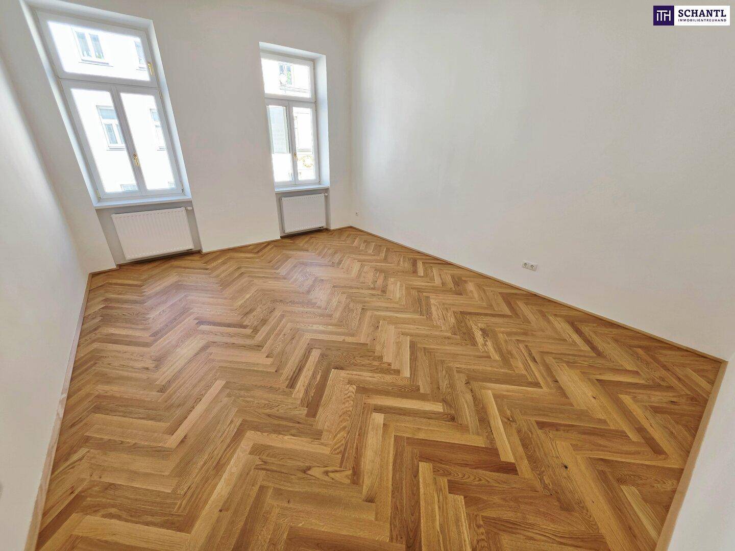 Großzügiges Zimmer mit Fischgrätparkett und hohen Fenstern, das viel Helligkeit bietet.