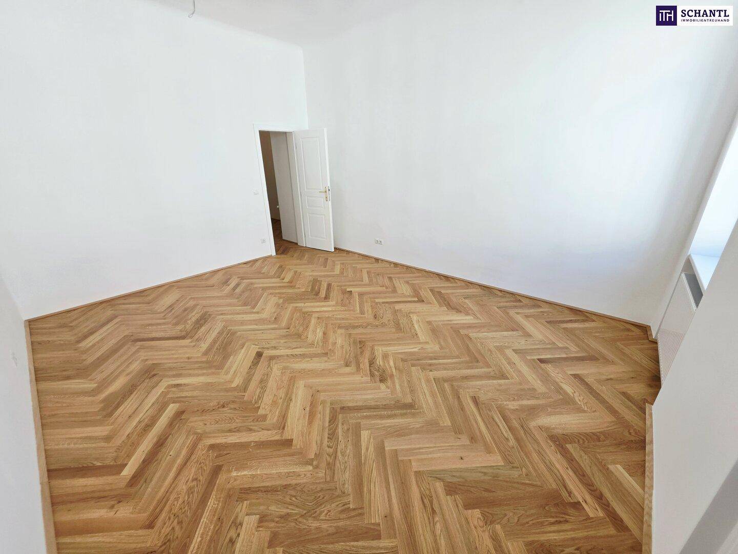 Leerer Raum mit elegantem Fischgrätparkett und weiß gestrichenen Wänden, bereit zur individuellen Gestaltung.