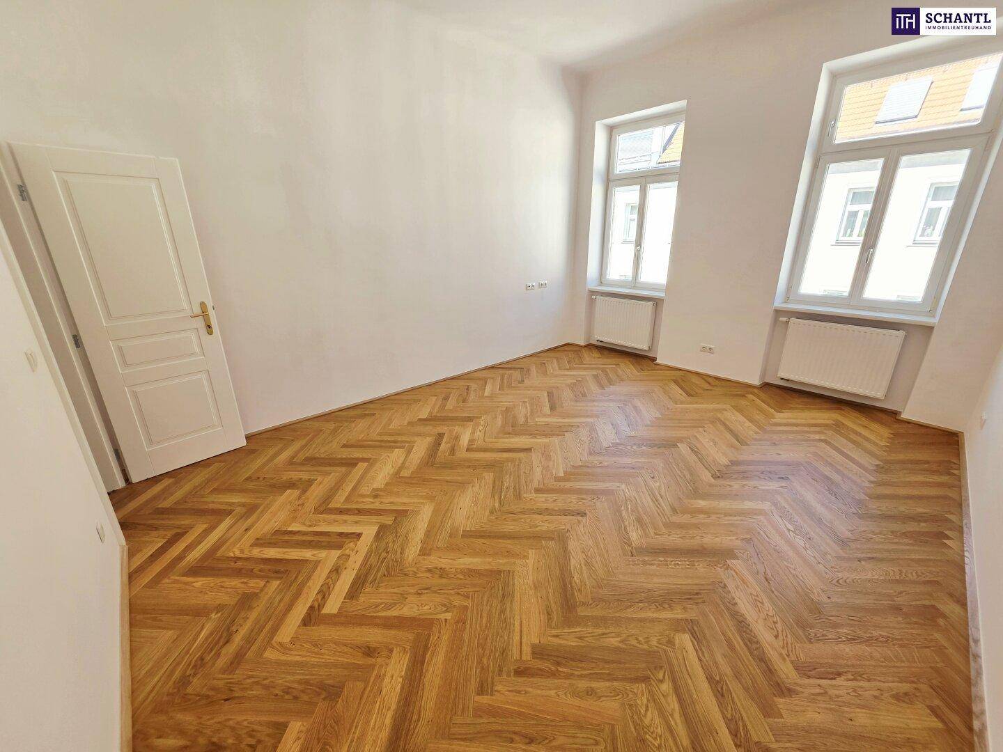 Renoviertes Zimmer mit Fischgrätparkett, zwei Fenstern und einer weißen Tür, sehr hell.