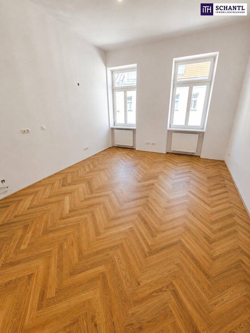 Großzügiges Zimmer mit klassischem Fischgrätparkett und zwei hohen Fenstern für viel Licht.