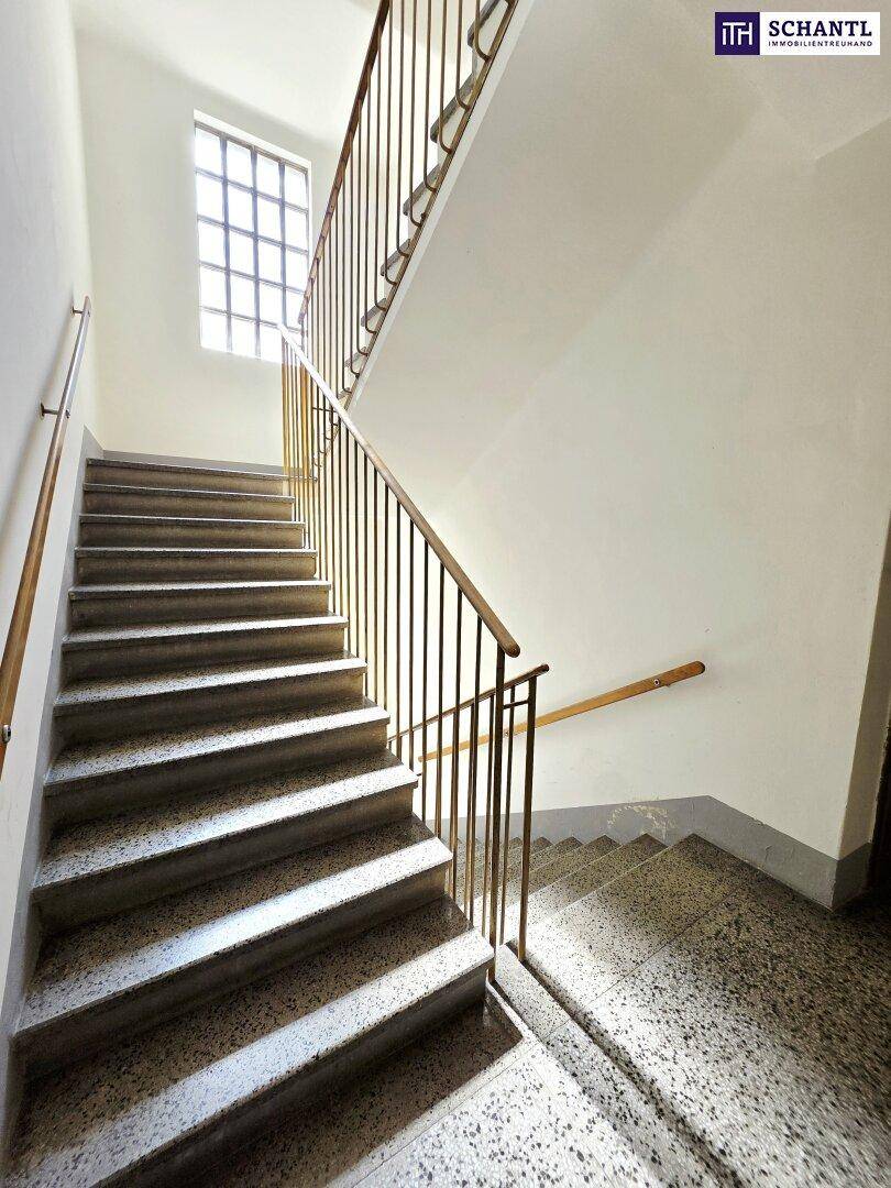 Treppenhaus mit Steinstufen und klassischem Metallgeländer, gut beleuchtet durch ein Fenster.