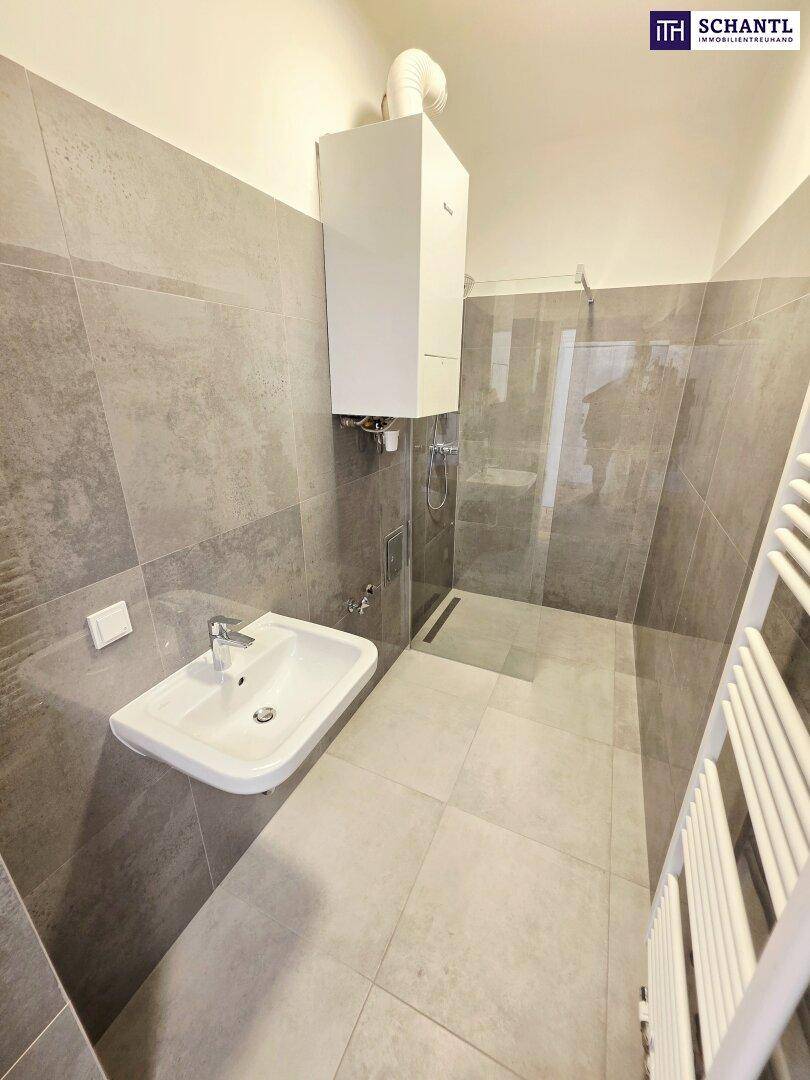 Modernes Badezimmer mit grauen Fliesen, Dusche, Waschbecken und Handtuchheizkörper.