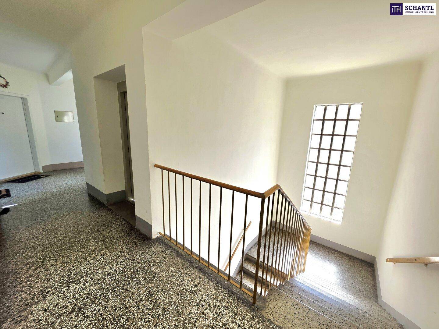 Treppenhaus mit Terrazzoboden, Metallgeländer und Fenster, inklusive Zugang zum Aufzug.