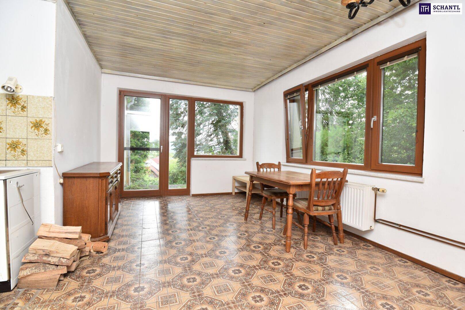 Geräumige Küche mit Essbereich, Holzofen und großen Fenstern, die viel Tageslicht hereinlassen.