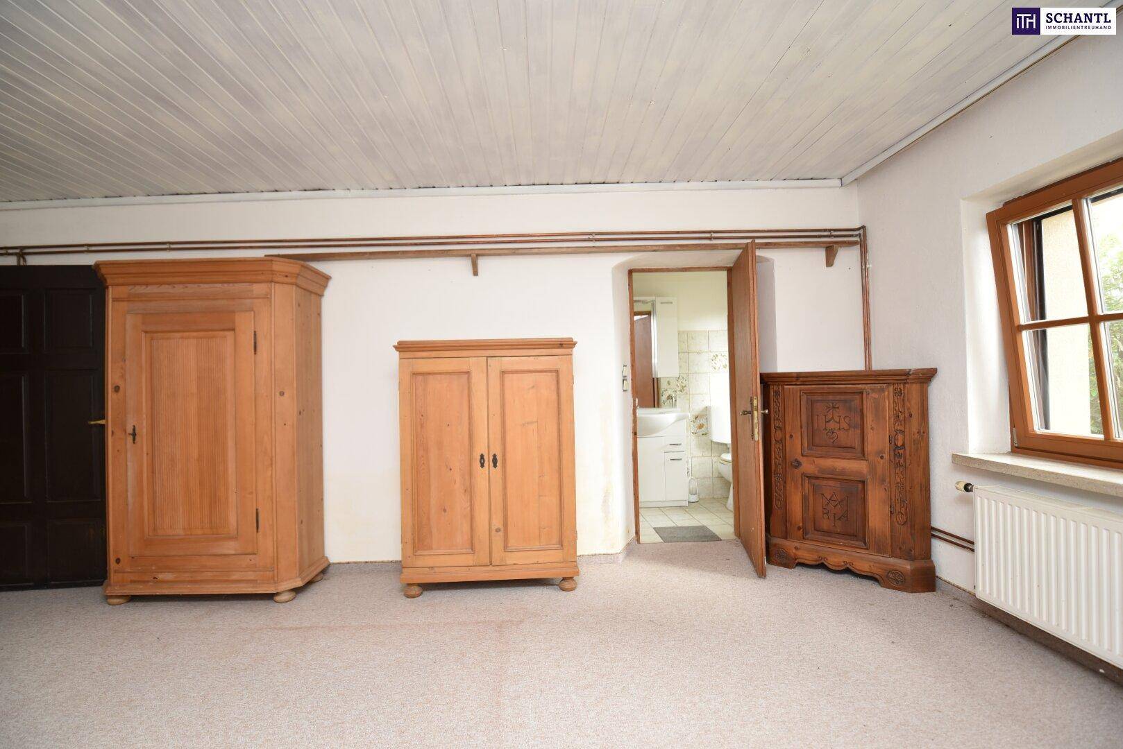 Schlafzimmer mit Zugang zu einem Badezimmer, ausgestattet mit traditionellen Holzschränken.