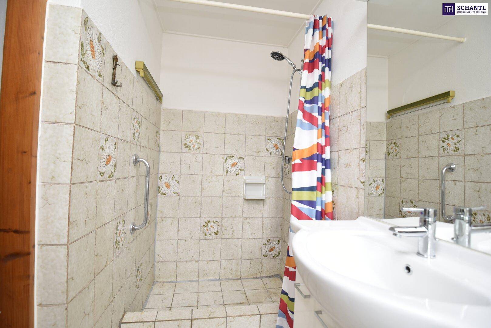 Badezimmer mit Duschbereich, Waschbecken und hellen Fliesen, ausgestattet mit Haltegriffen.