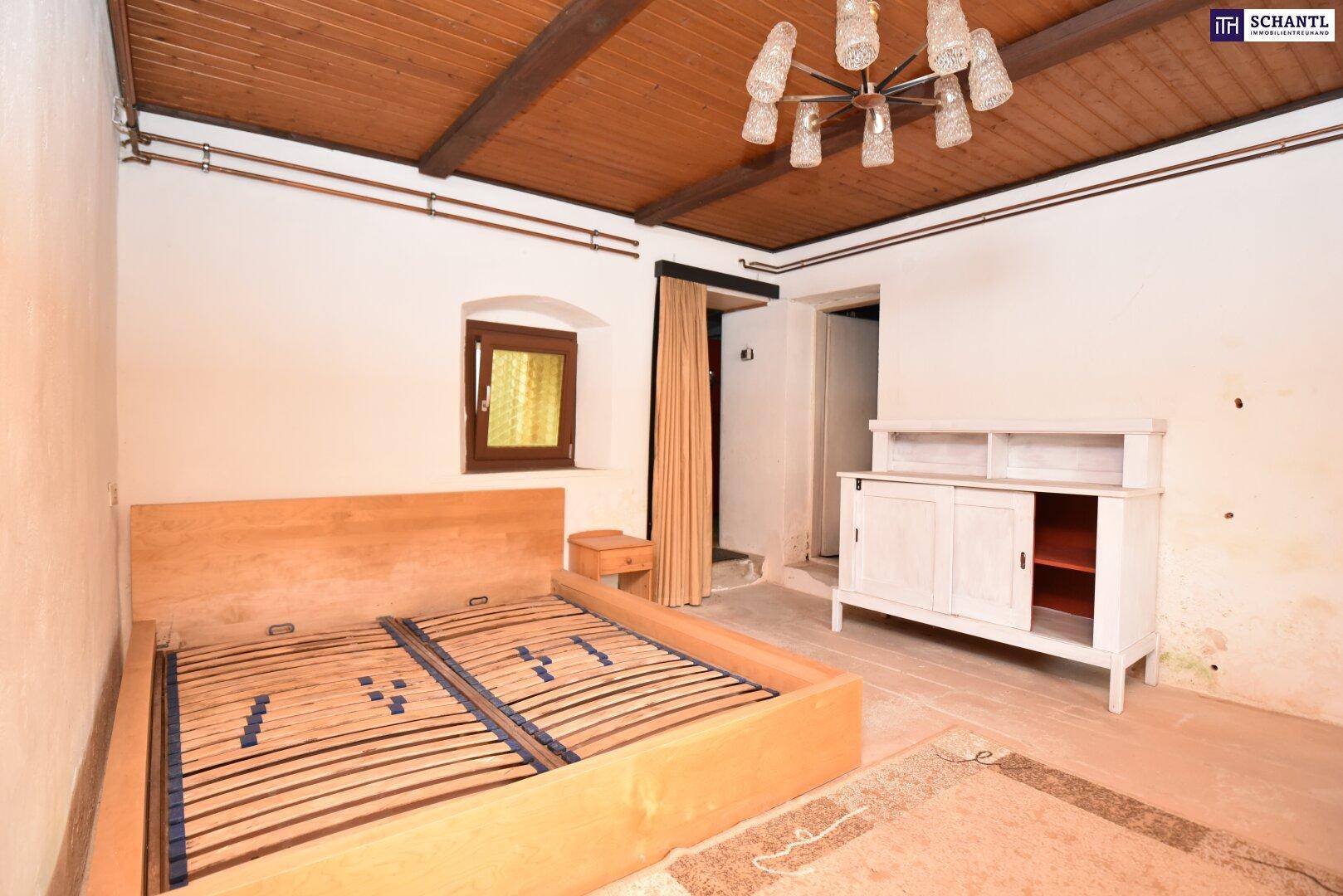 Schlafzimmer mit Holzbalkendecke, Holzbettrahmen und einem kleinen Fenster, das Licht spendet.
