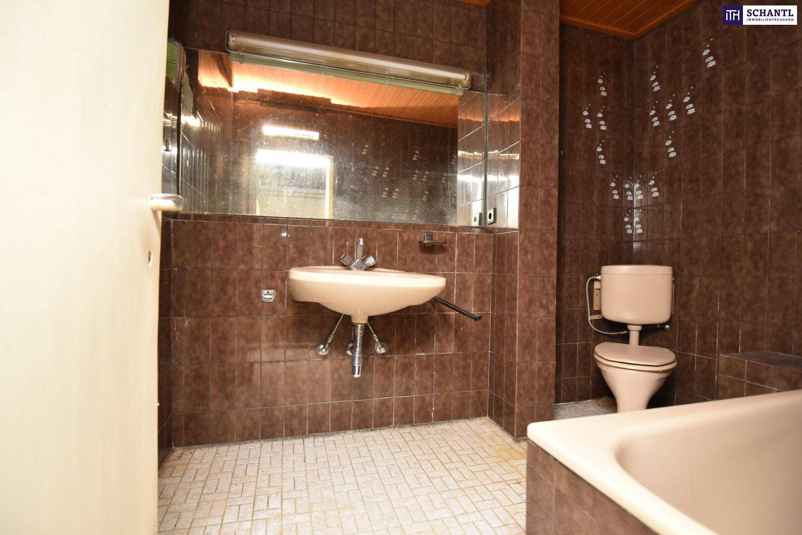 Dunkles Badezimmer mit braunen Fliesen, Waschbecken und Toilette, im Stil der 80er Jahre.