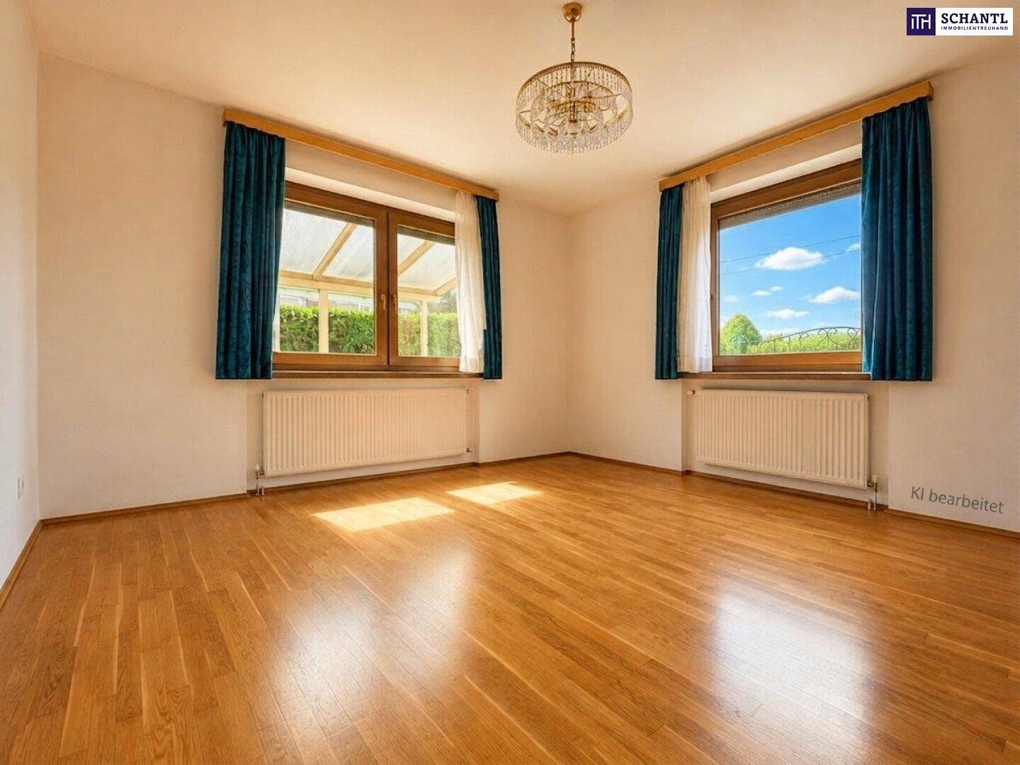 Helles Schlafzimmer mit Holzboden, zwei Fenstern und Blick ins Grüne sowie auf einen Wintergarten.