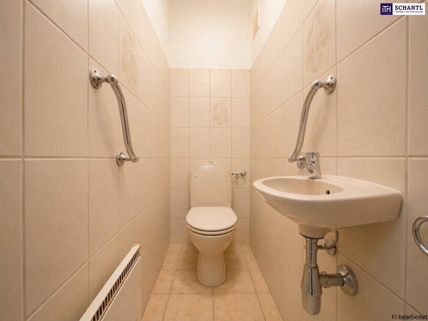 Gäste-WC mit beigefarbenen Fliesen, Toilette, Waschbecken und Haltegriffen.