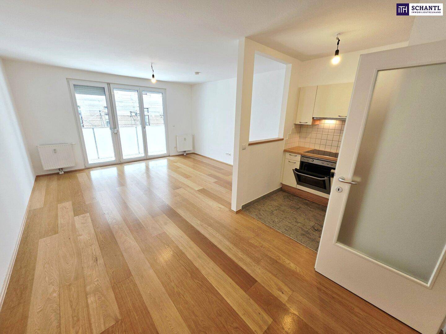 Offener Wohnbereich mit Holzboden und integrierter Küchenzeile, mit Balkonzugang.