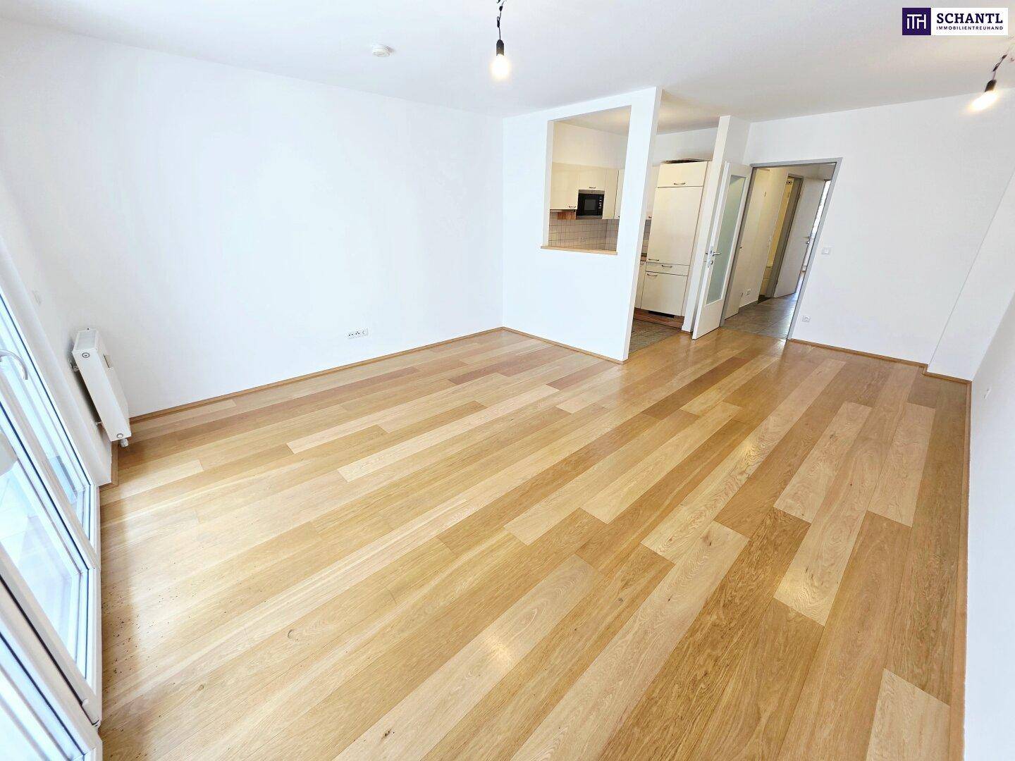 Weitläufiges Wohnzimmer mit Holzboden und direktem Zugang zur Küchenzeile.